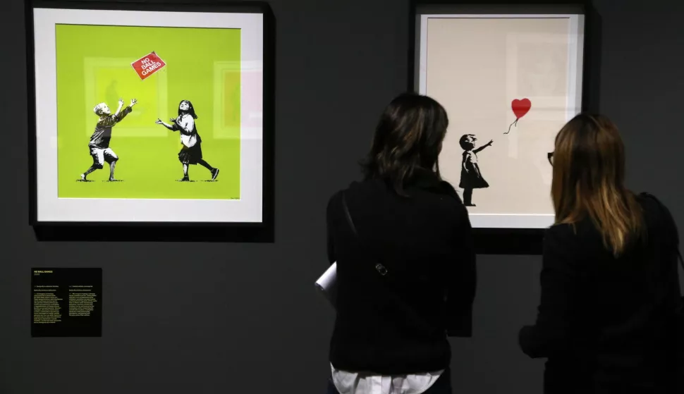 epa07179563 Two girls take a picture of the artworks "No ball games (green) 2009 " (L) and "Girl with red balloon" 2017 on display as part of the exhibition "A visual Protest. The art of Banksy" displayed at Mudec Museum in Milan, Italy, 20 November 2018. The exhibition runs from 21 November to 14 April 2019. EPA/MATTEO BAZZI
