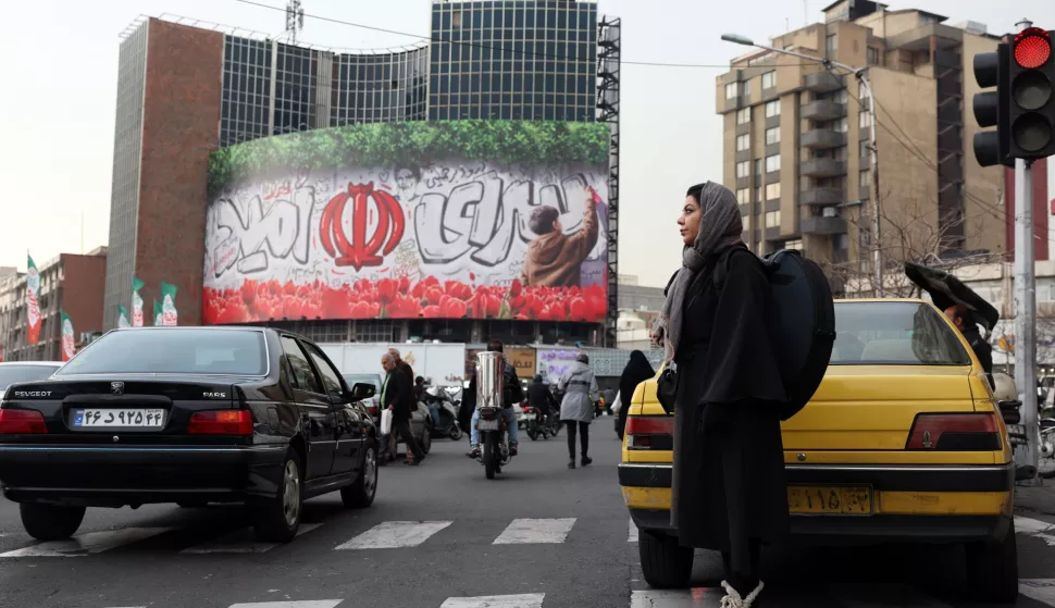 epa11876704 A woman waits to cross a street near a banner depicting Iran's national flag and a sentence reading in Persian 'Hope land' at the Valiasr square in Tehran, Iran, 05 February 2025. EPA/ABEDIN TAHERKENAREH