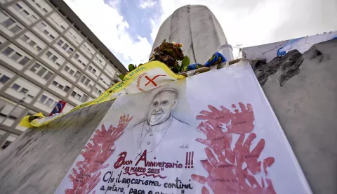 epa11960421 A banner celebrating the 12th anniversary of Pope Francis' pontificate is seen at the statue of John Paul II at the entrance of Gemelli Hospital where Pope Francis is still hospitalized, Rome, Italy, 13 March 2025. EPA/RICCARDO ANTIMIANI
