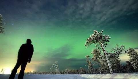 epa11150614 A person watches the northern lights (aurora borealis) illuminate the sky above the village of Akaslompolo in Kolari, beyond the Arctic Circle, Lapland, Finland, 13 February 2024. EPA/LAURENT GILLIERON