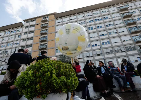 epa11982632 People sit under the statue of late Pope John Paul II outside Agostino Gemelli Hospital, where Pope Francis is hospitalized, in Rome, Italy, 23 March 2025. Pope Francis will be discharged on 23 March with a prescription of at least two months of convalescence after spending more than five weeks in the hospital for bilateral pneumonia. EPA/GIUSEPPE LAMI