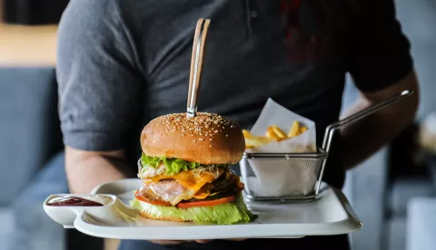 man holding plate with beef burger lettuce cheese tomato cucumber egg french fries sauce side view