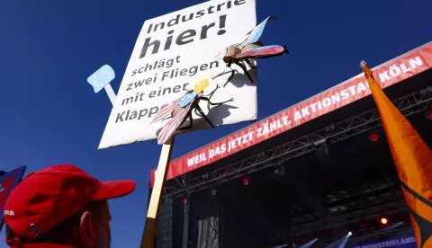 epa11965685 A participant holds a sign reading 'Industry here, kills two birds with one swatter' during a rally organized by the IG Metall trade union in Cologne, Germany, 15 March 2025. IG Metall has called for a nationwide day of protest, urging the incoming federal government to implement measures that would improve conditions for the industry. EPA/CHRISTOPHER NEUNDORF