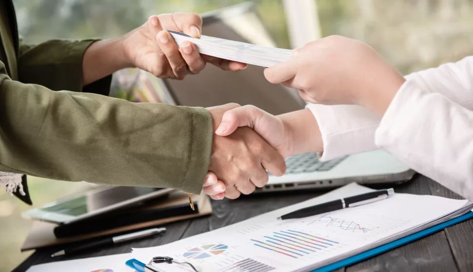 Business people shaking hands, finishing up meeting. businessman giving money to his partner while making contract - bribery and corruption concepts.banka novac kredit ilustracija freepik