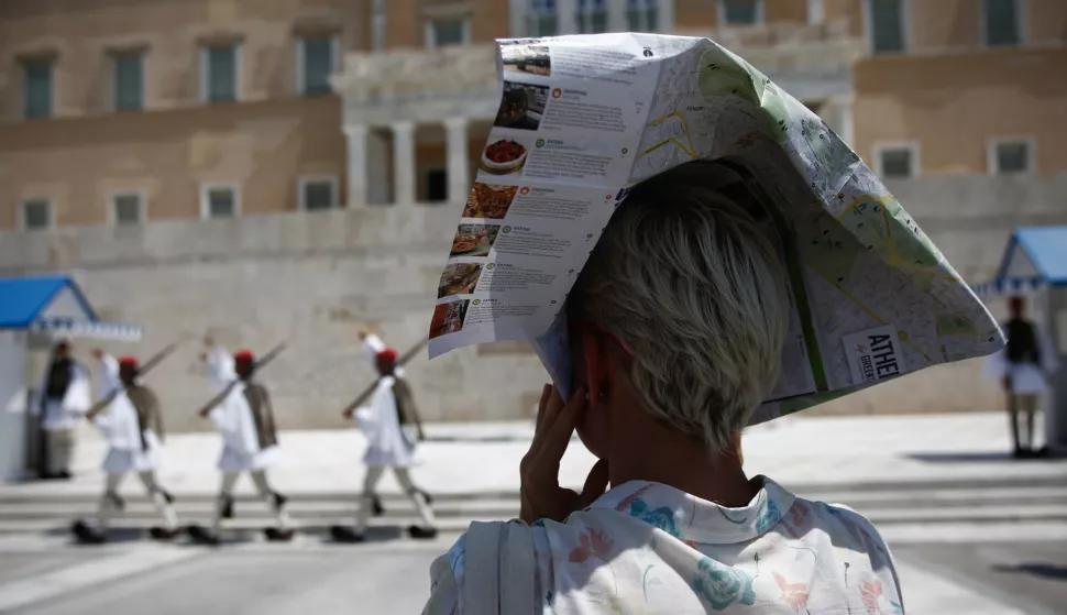 epa09385487 A woman covers head with a tourist flyer of Athens to protect herself from the sun as Greek Presidential Guard perform during a heatwave in central Athens, Greece, 01 August 2021. Temperatures are expected to reach up to 44 degrees Celsius in mainland Greece in the coming days, the National Meteorological Service (EMY) has warned the public in an emergency bulletin. EPA/YANNIS KOLESIDIS