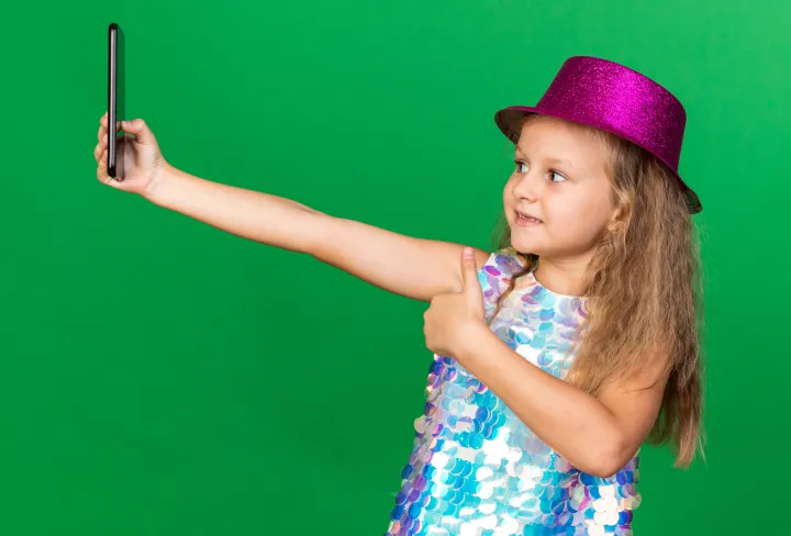 smiling little blonde girl with purple party hat thumbing up taking selfie on phone isolated on green background with copy spaceIako društvene mreže omogućuju povezivanje, izražavanje i informiranost, sve je više pokazatelja da njihova pretjerana uporaba dovodi do emocionalnih teškoća, gubitka samopouzdanja, zavisti, kroničnog uspoređivanja s drugima te raznih rizičnih oblika ponašanja, tvrde u Psihološkom centru, dodajući kako su sadržaji kojima su mladi izloženi na društvenim mrežamau vrlo često dorađeni, nerealni i orijentirani na stvaranje dojma savršenstvafreepik