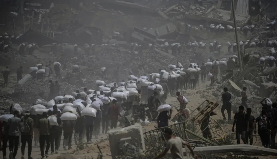 epa12265983 Internally displaced Palestinians carry bags of flour near a food distribution point in Zikim, northern Gaza Strip, 27 July 2025. The Israeli army declared a 'tactical pause' in military operations in parts of the Gaza Strip on 27 July, to facilitate the safe passage of humanitarian aid convoys. More than 130 Palestinians, the majority of whom children, have died of malnutrition in the Gaza Strip, the Palestinian Ministry of Health said on 27 July. EPA/MOHAMMED SABER