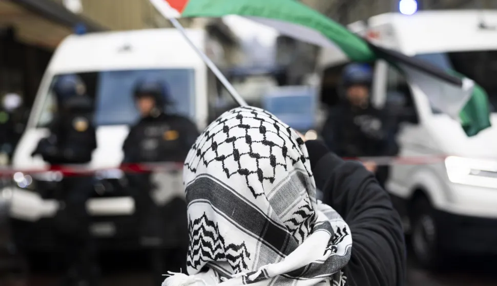 epa12447112 A protester wearing a keffiyeh and waving a Palestinian flag faces police officers during an unauthorized rally in solidarity with the Palestinian people, in Bern, Switzerland, 11 October 2025. EPA/PETER KLAUNZER
