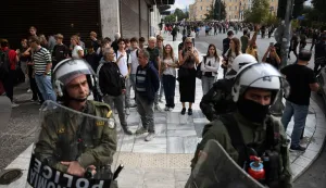 epa12452775 Tourists are pictured along with riot police officers during a demonstration of a 24-hour nationwide general strike, in Athens, Greece, 14 October 2025. The Athens Labor Center (EKA) and the Civil Servants' Confederation (ADEDY) are staging a 24-hour general strike in response to the provisions of the new labor bill being debated in Parliament, which establishes the '13-hour workday. EPA/GEORGE VITSARAS