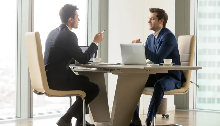 Two handsome businessmen sitting in comfortable chairs at desk with laptops in meeting room. CEO making important negotiation about companies partnership or corporate merger. Financiers planning dealpoduzetnik, gospodarstvenik, biznismen, sastanak, banka, novac, kredit, odjelo, poslovni izgled, posao, financije, ilustracija, freepik