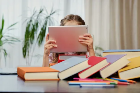 Little girl looking at the tablet PC in a classroom. Colorful books at the table.dijete skola učenik učenica tablet tehnologija računalo digital ilustracijafreepik