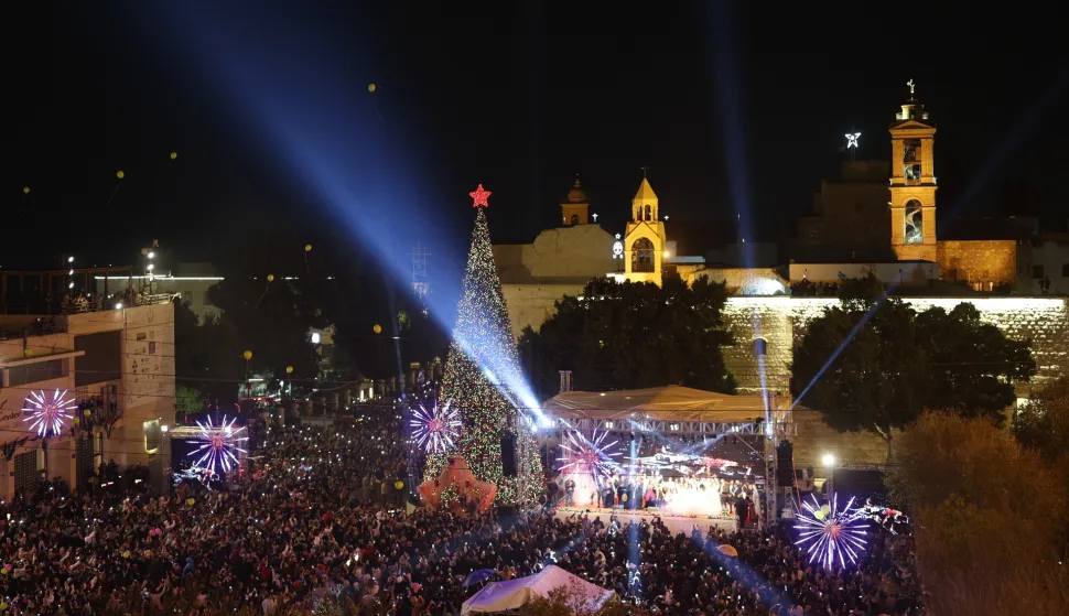 epa12575242 People gahter during the lighting of the Christmas tree ceremony at the Manger Square, next to the Church of Nativity in the background, in the West Bank city of Bethlehem, 06 December 2025. EPA/ATEF SAFADI