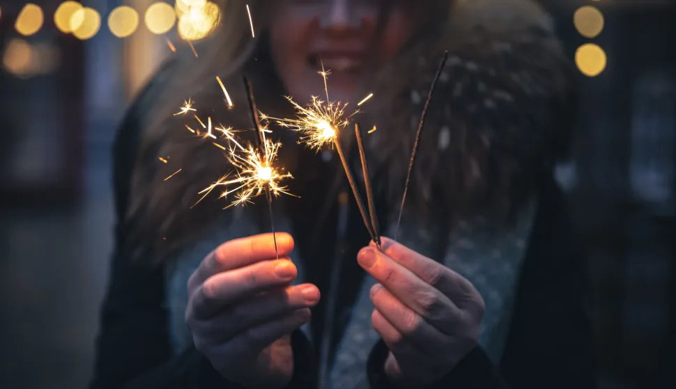 Burning sparklers in the hands of a young woman in the dark, outside, on a blurred background with bokeh.vatromet prskalice nova godina ilustracijafreepik