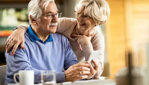 Senior man text messaging on mobile phone while wife is talking to him at home.