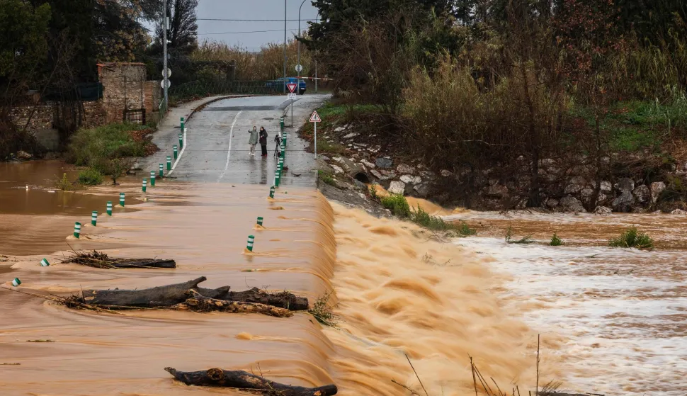 Pedestrians walk next to a flooded road due to the overflowing of the Agly river at the entrance of Rivesaltes in the Pyrenees-Orientales department in south-western France on December 26, 2025. Aude, Pyr?n?es-Orientales and Haute-Corse have been placed on orange alert for rain?flooding or floods by M?t?o-France until midnight on December 26, 2025. (Photo by Jean-Christophe MILHET/AFP)