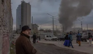 AFP PICTURES OF THE YEAR 2025Pedestrians walk at a flea market as smoke rises in the distance following the Russian missile attack, in Kyiv on April 6, 2025, amid the Russian invasion of Ukraine.. Kyiv Mayor said the city was under missile attack on April 6, 2025 with explosions in the Ukrainian capital, two days after a Russian missile killed 18 people in Ukraine's President's hometown. (Photo by Roman PILIPEY/AFP)/AFP PICTURES OF THE YEAR 2025