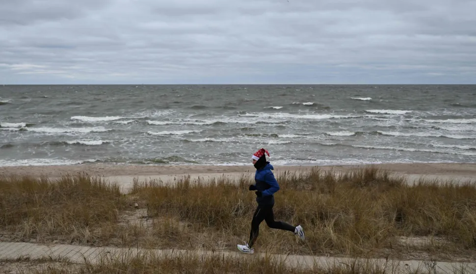 A woman wearing a Santa Claus hat runs along the Baltic Sea beach in Klaipeda, Lithuania on December 25, 2025. (Photo by Sergei GAPON/AFP)