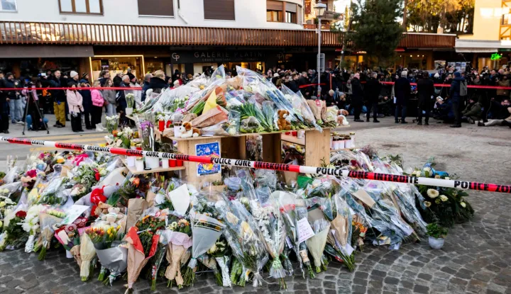 Flowers and candles in tribute to the victims are displayed at a makeshift memorial following a fire at "Le Constellation" bar during New Year's Eve celebrations, killing 40 people and injuring 119, in the Alpine ski resort town of Crans-Montana, on January 3, 2026. Swiss investigators worked on January 3 to identify the victims and exact cause of the blaze that killed 40 New Year revellers at a packed bar in the ski resort of Crans-Montana. Dozens of people badly burnt in the fire early on January 1 in the glitzy Alpine town were taken to nearby countries for urgent treatment, while authorities pointed the finger at lit sparklers attached to champagne bottles igniting foam on the ceiling. Most of the 119 people wounded in the fire remained in critical condition. (Photo by JEAN-CHRISTOPHE BOTT/POOL/AFP)