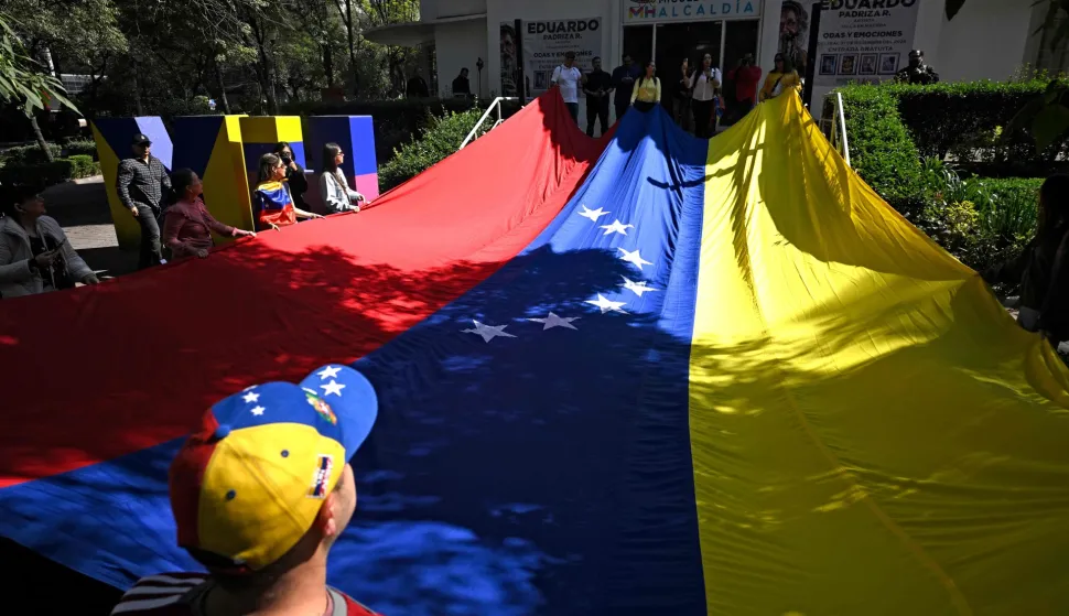Venezuelans living in Mexico gather to celebrate with a giant national flag at the Lincoln Park in the Polanco neighborgood, in Mexico City, on January 4, 2026, a day after Venezuela's leader Nicolas Maduro was captured in a US strike. Venezuela's military on Sunday recognized Delcy Rodriguez, deputy to ousted president Nicolas Maduro, as the country's acting leader, after US forces extracted the former head of state to face trial. (Photo by Alfredo ESTRELLA/AFP)