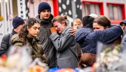 TOPSHOT - Mourners gather near the bar Le Constellation where a fire ripped through the venue during New Year's celebrations in the Alpine ski resort town of Crans-Montana killing around 40 people and injuring more than 100 others, in Crans-Montana on January 2, 2026. Investigators raced on January 2, 2026 to identify the victims of a fire that ripped through a bar in the Swiss Alps town of Crans-Montana, turning a New Year's celebration into one of the country's worst tragedies. Frederic Gisler, police commander in the Wallis canton in southwestern Switzerland, told reporters that authorities had counted "around 40 people who have died and around 115 injured, most of them seriously". (Photo by MAXIME SCHMID/AFP)