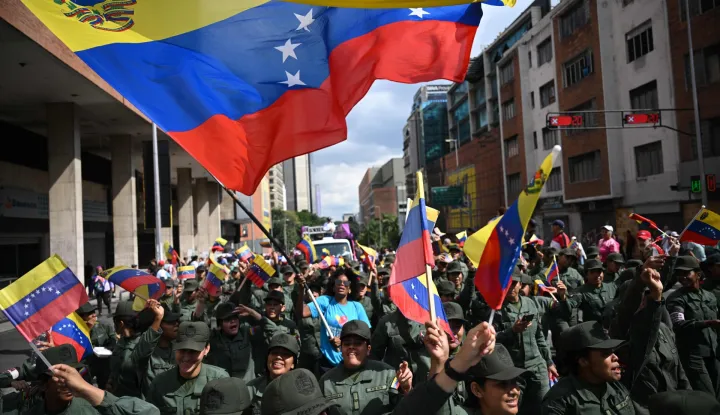 A woman waves a Venezuelan flag among members of the National Bolivarian Armed Forces during a rally in support of ousted Venezuela's President Nicolas Maduro and his wife Cilia Flores in Caracas on January 6, 2026. US forces killed 55 Venezuelan and Cuban military personnel during their stunning raid to capture Nicolas Maduro, tolls published by Caracas and Havana showed on January 6. (Photo by Federico PARRA/AFP)