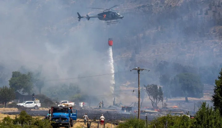 A helicopter sprays water to extinguish a bushfire in Mount Pirque at El Hoyo, in the Patagonian region of Chubut province, Argentina on January 10, 2026. More than 5,500 hectares of forest have been consumed by the main wildfire in Argentina's Patagonia, as hundreds of firefighters and local volunteers struggled to contain flames out of control that have left small communities on edge. The blazes come a year after Patagonia suffered its worst wildfires in three decades, part of a string of extreme events that has kept official and community firefighting systems under constant strain. (Photo by Gonzalo KEOGAN/AFP)