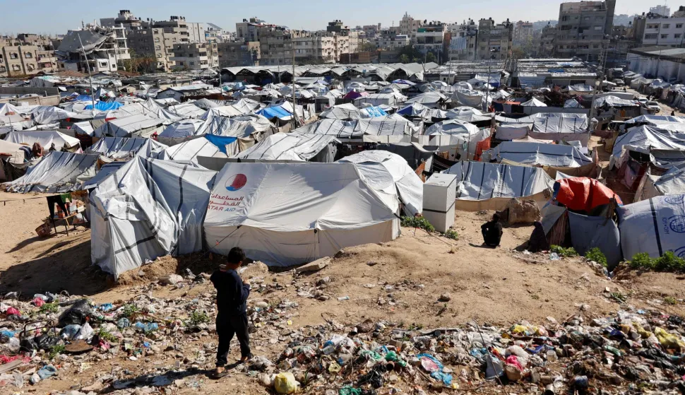 A child walks past garbage towards tent shelters housing displaced Palestinian families are set-up on empty land in Gaza City on January 11, 2026. The majority of Gaza's 2.4 million people have been displaced, often multiple times, by the war that began with Hamas's attack on southern Israel on October 7, 2023. With displaced families living in tented camps, a serious concerns has been raised over their living conditions. (Photo by Omar AL-QATTAA/AFP)