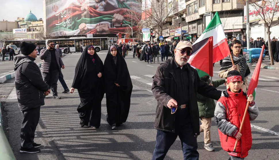 People walk past a large patriotic banner depicting the Iranian flag on Enghelab Square in Tehran on January 14, 2026. Iran on Januray 14 vowed fast-track trials for people arrested over a massive wave of protests, after US President Donald Trump threatened "very strong action" if the Islamic republic goes ahead with hangings. In Tehran, authorities held a funeral ceremony for over 100 members of the security forces and other "martyrs" killed in the demonstrations, which authorities have branded as "riots" while accusing protesters of waging "acts of terror". (Photo by ATTA KENARE/AFP)