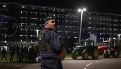 A french riot police officer stands in front of tractors parked outside Toulouse airport in Toulouse, southwestern France on January 14, 2026 in protest against the government's mandatory culling protocol for cattle herds affected by lumpy skin disease (dermatose nodulaire contagieuse) and the EU-Mercosur trade deal. (Photo by Ed JONES/AFP)