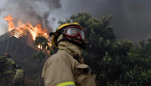 Firefighters try to extinguish a burning house during a wildfire in Concepcion, Chile, on January 18, 2026. Chilean President Gabriel Boric declared a state of emergency on January 18 for two southern regions where raging wildfires have forced about 20,000 people to evacuate their homes. (Photo by GUILLERMO SALGADO/AFP)