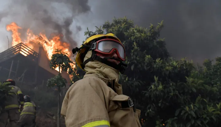 Firefighters try to extinguish a burning house during a wildfire in Concepcion, Chile, on January 18, 2026. Chilean President Gabriel Boric declared a state of emergency on January 18 for two southern regions where raging wildfires have forced about 20,000 people to evacuate their homes. (Photo by GUILLERMO SALGADO/AFP)