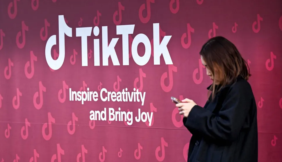 A woman uses her phone in front of Tiktok's booth during the World Economic Forum (WEF) annual meeting in Davos on January 19, 2026. The World Economic Forum takes place in Davos from January 19 to January 23, 2026. (Photo by INA FASSBENDER/AFP)