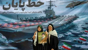 Women pose with a poster depicting Iran's supreme leader Ayatollah Ali Khamenei as they stand before a banner depicting a US Navy aircraft carrier with US-flag-wrapped coffins on the deck, during a rally marking the 47th anniversary of the 1979 Islamic revolution in Tehran on February 11, 2026. The Persian calendar date of Bahman 22 celebrates the anniversary of the resignation of the ousted shah's last prime minister and the formal assumption of power by revolutionary leader Ayatollah Ruhollah Khomeini. (Photo by AFP)