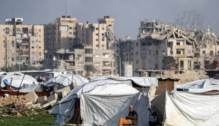 A man sits outside tent shelters near damaged buildings at the Maghazi camp for Palestinian refugees in the central Gaza Strip on February 11, 2026. Since October 10, a fragile US-sponsored truce in Gaza has largely halted the fighting between Israeli forces and Hamas, but both sides have alleged frequent violations. (Photo by Eyad BABA/AFP)