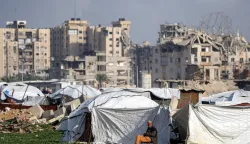 A man sits outside tent shelters near damaged buildings at the Maghazi camp for Palestinian refugees in the central Gaza Strip on February 11, 2026. Since October 10, a fragile US-sponsored truce in Gaza has largely halted the fighting between Israeli forces and Hamas, but both sides have alleged frequent violations. (Photo by Eyad BABA/AFP)