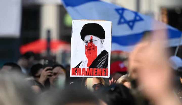 TOPSHOT - A placard featuring a picture of Iran's Supreme Leader Ayatollah Ali Khamenei with a hand gesture painted on it in red is seen during a demonstration "Freedom for Iran" at the square Potsdamer Platz in Berlin, Germany on February 28, 2026. The United States and Israel launched strikes against Iran on February 28, sparking fears of regional war with explosions reported across the Middle East as the Islamic republic retaliated with barrages of missiles. (Photo by RALF HIRSCHBERGER/AFP)