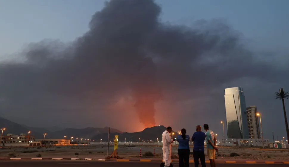 Foreign workers look at a tall plume of black smoke ascends following an explosion in the Fujairah industrial zone on March 3, 2026. Iran's strikes on Gulf neighbours since February 28, following the US-Israeli attack, forced the UAE to shut its airspace, blindsiding travellers who thought they were headed to one of the region's safest holiday destinations. (Photo by Fadel SENNA/AFP)