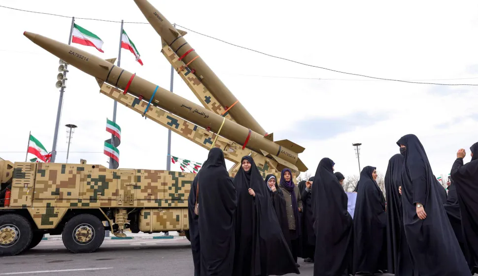 Women walk near ballistic missile launch vehicles in Tehran on February 11, 2026, during a rally marking the 47th anniversary of the 1979 Islamic revolution. The Persian calendar date of Bahman 22 celebrates the anniversary of the resignation of the ousted shah's last prime minister and the formal assumption of power by revolutionary leader Ayatollah Ruhollah Khomeini. (Photo by AFP)