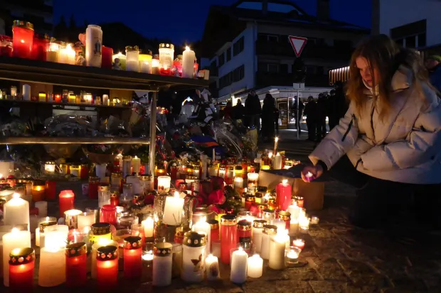 A woman displays a candle at a makeshift memorial following a fire at "Le Constellation" bar during New Year's Eve celebrations, killing 40 people and injuring 119, in the Alpine ski resort town of Crans-Montana, on January 3, 2026. Swiss investigators worked on January 3 to identify the victims and exact cause of the blaze that killed 40 New Year revellers at a packed bar in the ski resort of Crans-Montana. Dozens of people badly burnt in the fire early on January 1 in the glitzy Alpine town were taken to nearby countries for urgent treatment, while authorities pointed the finger at lit sparklers attached to champagne bottles igniting foam on the ceiling. Most of the 119 people wounded in the fire remained in critical condition. (Photo by Robin MILLARD/AFP)