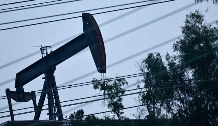 A pumpjack operates in the Montebello Oil Field behind a row of power lines on March 4, 2026 in Montebello, California. US and European stock markets advanced March 4 as oil prices steadied, after Asian bourses suffered deep losses amid inflation worries sparked by the US-Iran war. Markets have been roiled much of the week as the conflict between the US and Iran effectively closed shipping through the Strait of Hormuz, where a fifth of the world's crude oil travels as well as considerable liquefied natural gas (LNG) supplies travel through. (Photo by Frederic J. BROWN/AFP)