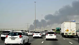 Smoke billows from an ongoing fire near Dubai International Airport as vehicles drive on a highway in Dubai on March 16, 2026. Flights were gradually resuming at Dubai airport on March 16, previously the world's busiest for international flights, the airport operator said, after a "drone-related incident" sparked a fuel tank fire nearby, as Iran kept up its Gulf attacks. (Photo by AFP)/