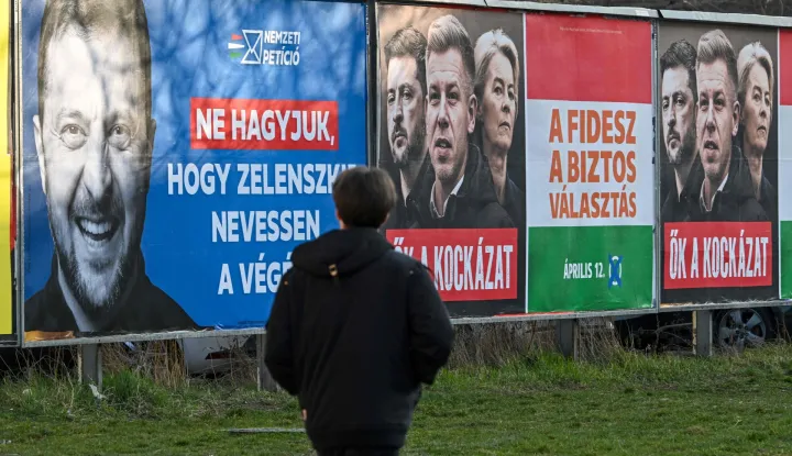 (FILES) A woman walks past a pro-government billboard featuring a portrait of Ukrainian President Volodymyr Zelensky (L), with the lettering reading, 'Let's not let Zelensky have the last laugh', and another billboard featuring European Commission President Ursula von der Leyen (R), Ukraine's President Volodymyr Zelensky (C), and Hungarian opposition leader Peter Magyar (L) with the lettering reading 'They themselves are the risk' in Budapest's 3rd district on March 3, 2026, in prepatation for the upcomping general election set to take place on April 12, 2026. Hungary's long-time premier Viktor Orban and his main opponent Peter Magyar are set to stage rival marches in Budapest on Sunday, March 15, 2026, both pushing allegations of foreign interference four weeks before the elections. (Photo by Attila KISBENEDEK/AFP)
