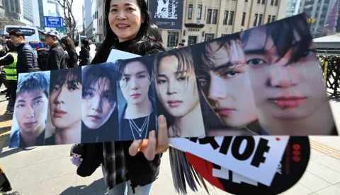A woman holds a banner showing pictures of BTS members as BTS fans arrive at the venue of the comeback concert of K-pop boy group BTS in downtown Seoul on March 21, 2026. The world's biggest boy band BTS reunites on March 21, for an open-air comeback concert in the heart of Seoul, expected to draw around 250,000 people and beamed live across the globe. (Photo by Jung Yeon-je/AFP)