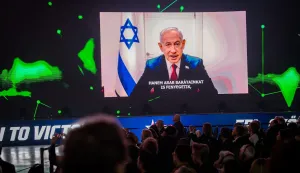 Participants watch and listen to a video message of Israeli Prime Minister Benjamin Netanyahu displayed on a screen during the Conservative Political Action Conference (CPAC) at a sports and cultural centre in Budapest, Hungary, on March 21, 2026. (Photo by Gergely BESENYEI/AFP)
