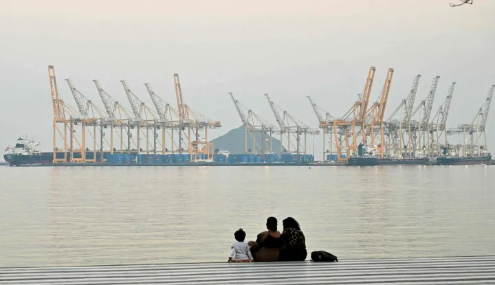 (FILES) A family sits against the backdrop of a dockyard off coast city of Fujairah, in the Strait of Hormuz in the northern Emirate on February 25, 2026. The US president sent a peace plan to Iran as he voiced optimism on March 25, 2026 at ending nearly a month of warfare, with Tehran announcing that it will let "non-hostile" oil vessels go through the crucial Strait of Hormuz. Oil prices dropped sharply and stocks in Asia rose on broader de-escalation hopes following nearly four weeks of war, as the US president appeared to be ramping up efforts to bring an end to his joint military operation with Israel. (Photo by Giuseppe CACACE/AFP)