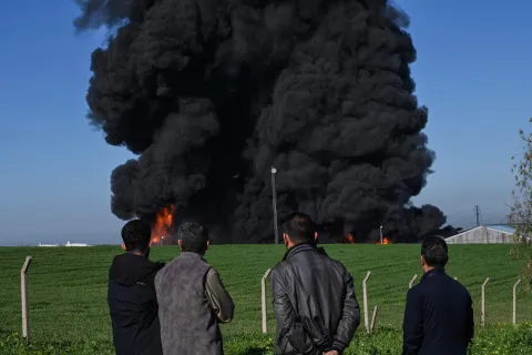 TOPSHOT - People watch as smoke billows from an oil warehouse in the Kani Qirzhala area on the outskirts of Erbil, the capital of Iraq's autonomous Kurdistan region, following a suspected drone strike, on April 1, 2026. Iraq has been drawn into the broader Middle East war that started with US-Israeli strikes on Iran on February 28. Erbil is home to a major US consulate complex, while its airport houses military advisers attached to a US-led anti-jihadist coalition. Regular drone attacks by pro-Iran armed groups have usually been intercepted by air defences. (Photo by AFP)