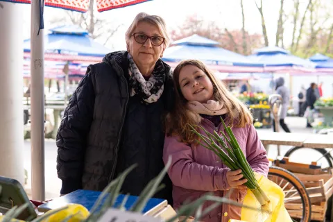 Osijek, 2. 4. 2026., TržnicaTržnica; ponuda; kupovina; voće; povrće; kupci; potro&scaron;ači; namirnice; nabavka; cijene; biljke; prodavačica; unuka; OPGSilva i njezina unuka Lucija