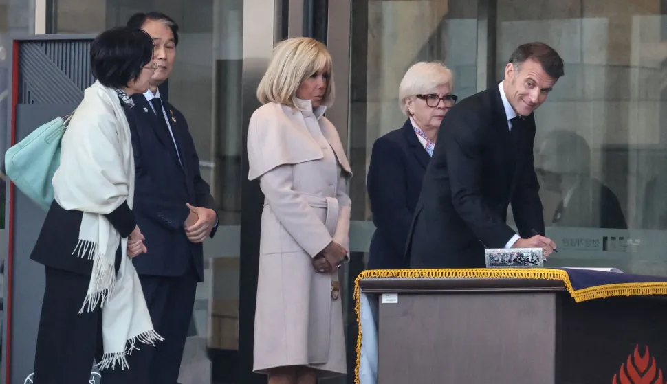 French President Emmanuel Macron (R) signs the guestbook during a visit at the War Memorial of Korea with his wife Brigitte Macron (C) and French Defence Minister Catherine Vautrin (2nd R) in Seoul on April 2, 2026. (Photo by Ludovic MARIN/POOL/AFP)