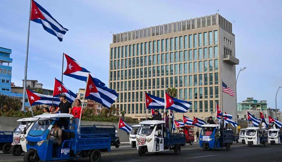 Cubans on electric tricycles decorated with Cuban flags ride past the US embassy during the anti-imperialist youth march in Havana on April 2, 2026. (Photo by YAMIL LAGE/AFP)