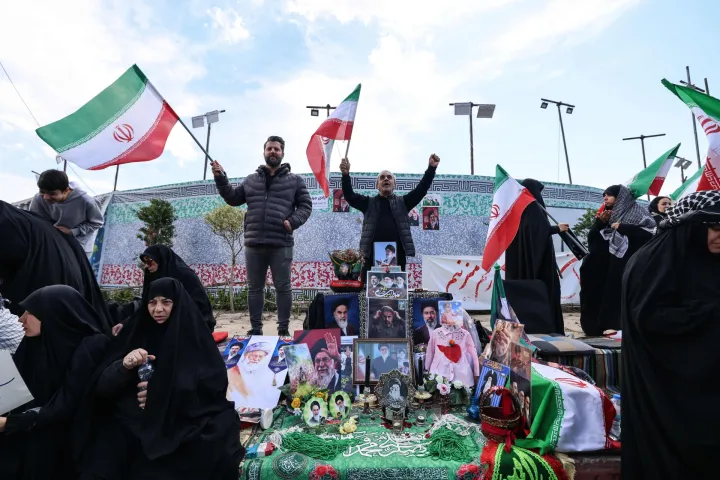 Iranians wave national flags next to a makeshift memorial as they gather in Tehran's Revolution Square after the United States and Iran agreed to a two-week ceasefire, on April 8, 2026. The United States and Iran agreed to a two-week ceasefire barely an hour before the US president's April 8 deadline to obliterate the country, triggering global relief alongside apprehension. (Photo by ATTA KENARE/AFP)/